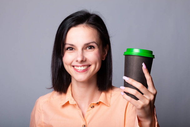 cute girl in an orange shirt holds a cup of coffee in her hands, gray background - Fotó, kép