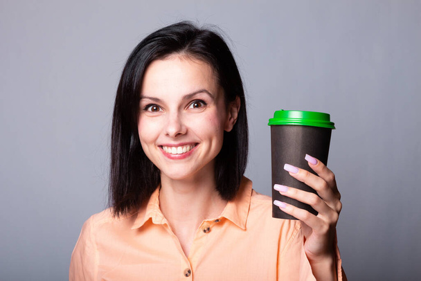 linda dama en una camisa naranja sostiene una taza de café en sus manos, fondo gris - Foto, imagen