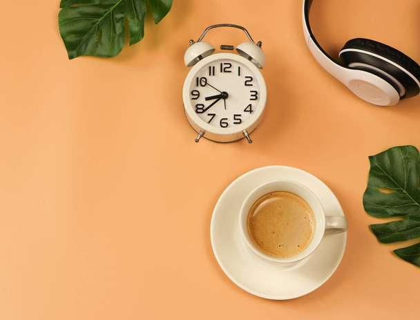 Bovenaanzicht of platte lay-out van koffiebeker, vintage wekker en koptelefoon op oranje achtergrond met kopieerruimte. Positieve ochtend routine concept. - Foto, afbeelding