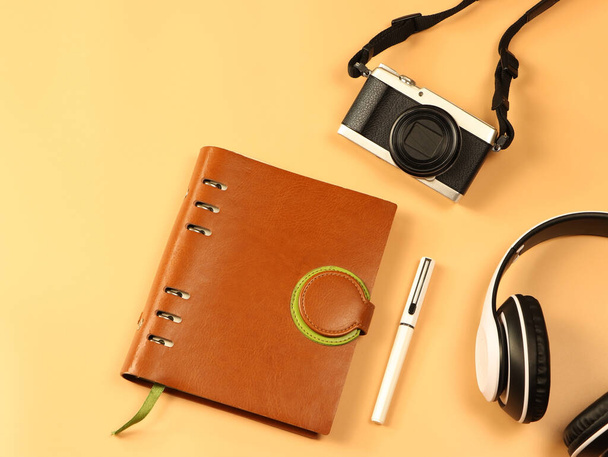 Bovenaanzicht of platte lay-out van vintage camera, hoofdtelefoon en notebook op oranje achtergrond met kopieerruimte. Freelance, creatief, reizend tijdschriftconcept. - Foto, afbeelding