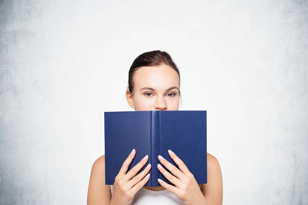 Portrait of young businesswoman standing with book over concrete wall background. Concept of knowledge - Fotoğraf, Görsel