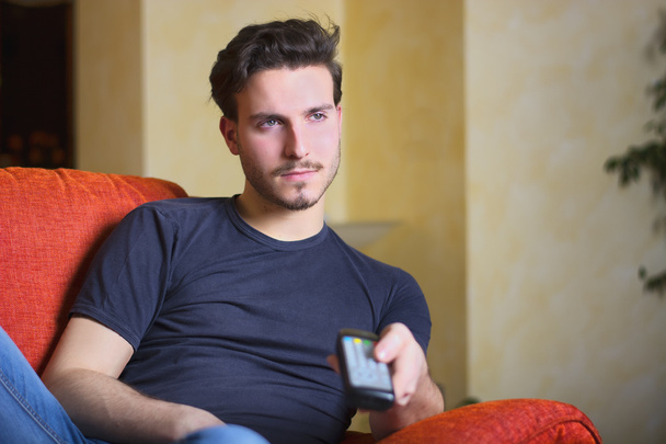 Handsome young man on counch, using TV remote control - Photo, image