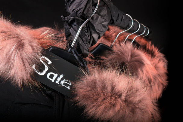 黒の冬のコートの多くは、黒の背景に服ラックに掛けフード付きの毛皮のジャケット、販売記号、黒の金曜日 - 写真・画像