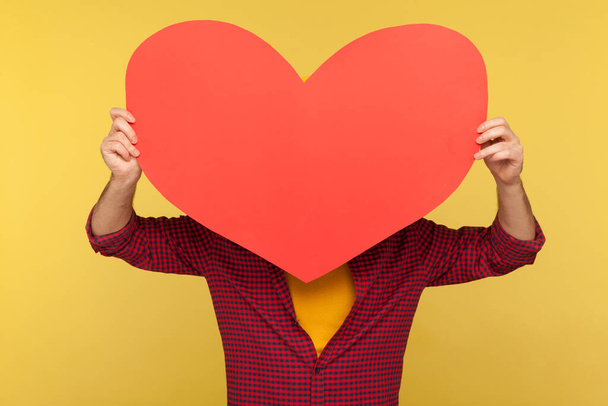 Anonymous person in checkered shirt hiding behind big red paper heart, holding symbol of love care, cardiac issues, demonstrating affection feelings with greeting card on Valentine's Day. isolated - Foto, immagini