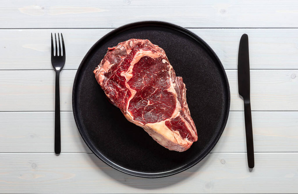 Raw beef rib eye steak. Organic farm meat. Black plate on wooden table - Foto, imagen