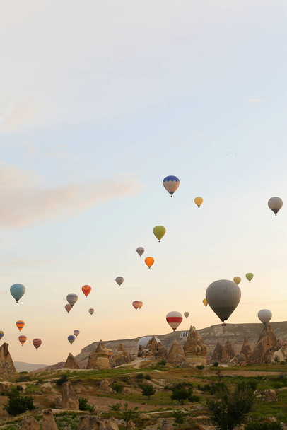 В Турции над скалами Каппадокии пролетает много больших воздушных шаров. - Фото, изображение