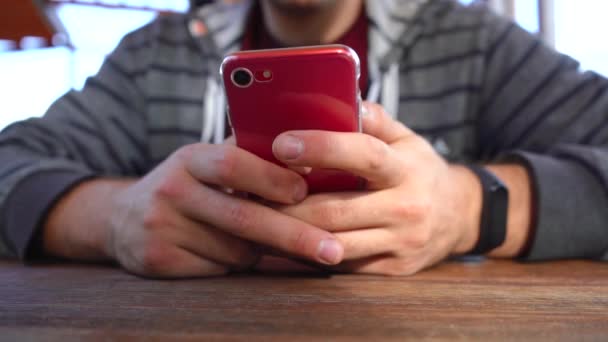 hombre utiliza un teléfono rojo mientras está sentado en una mesa - Imágenes, Vídeo
