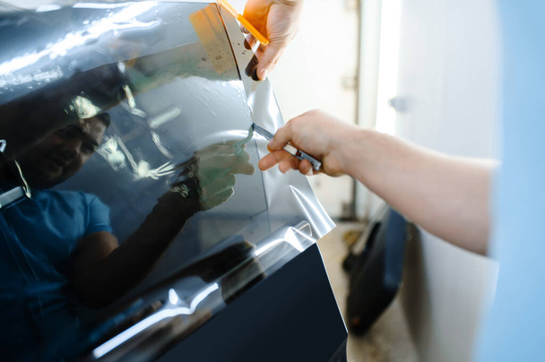 Männliche Verpackung hält Sonnenschutzfolie, Autotönservice. Arbeiter mit Vinylfarbe auf Autoscheibe in Garage, getöntes Autoglas - Foto, Bild