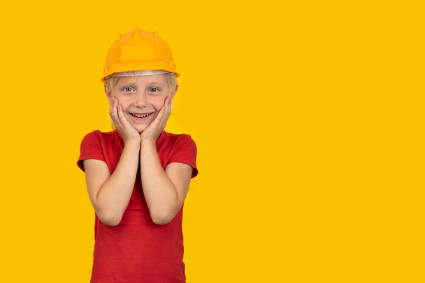 Joyful blond boy in hard hat on yellow background. Choice of specialty. - Photo, Image