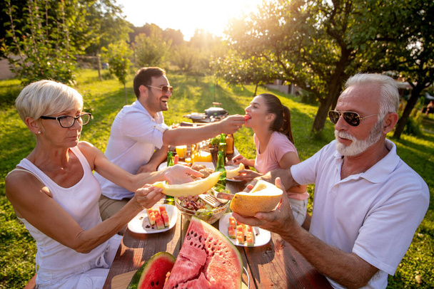 Deux générations de la famille s'amusent en déjeunant dans la nature. Loisirs, nourriture, personnes et vacances concept - Photo, image