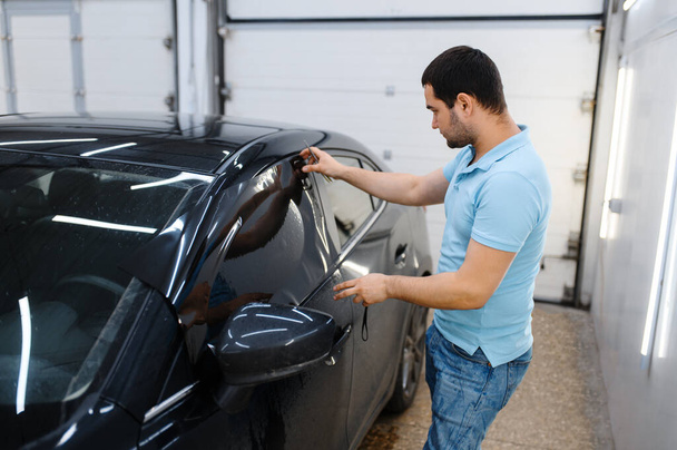 Male worker tries on wetted car tinting, tuning service. Mechanic applying vinyl tint on vehicle window in garage, tinted automobile glass - Photo, Image