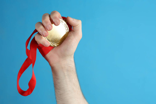 Man holding golden medal on blue background, closeup. Space for design - Foto, Imagen