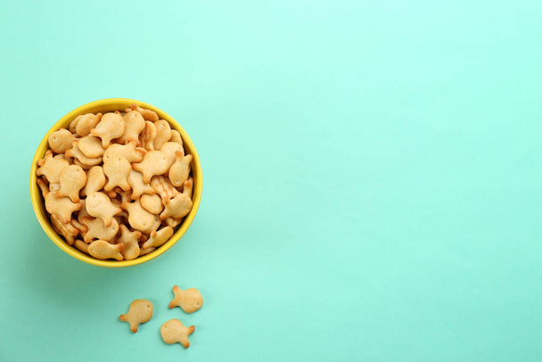 Delicious goldfish crackers in bowl on turquoise background, flat lay. Space for text - Valokuva, kuva