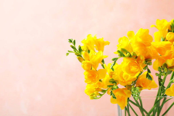 Beautiful blooming yellow freesias in glass vase against pink background. Space for text - Fotografie, Obrázek