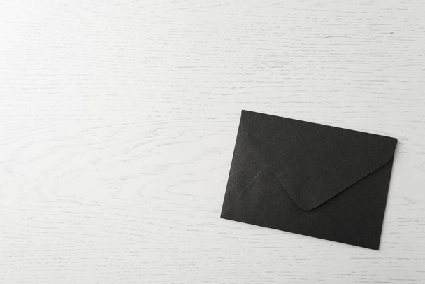 Black paper envelope on white wooden background, top view. Space for text - 写真・画像