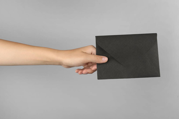 Woman holding black paper envelope on light grey background, closeup - Foto, imagen
