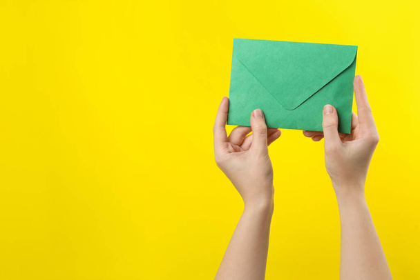 Woman holding green paper envelope on yellow background, closeup. Space for text - Foto, Imagen
