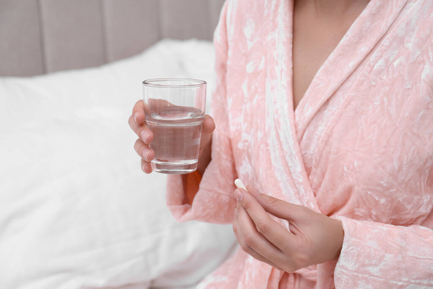Young woman with glass of water taking pill in bedroom, closeup - Foto, Imagem
