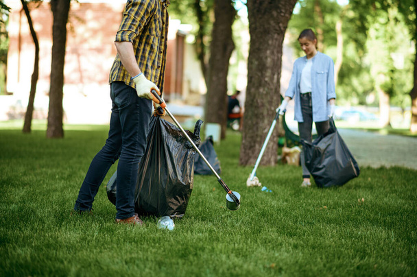 Two men collects plastic garbage in bags in park, volunteering. Male person cleans forest, ecological restoration, eco lifestyle, trash collection and recycling, ecology care, environment cleaning - Foto, Imagen