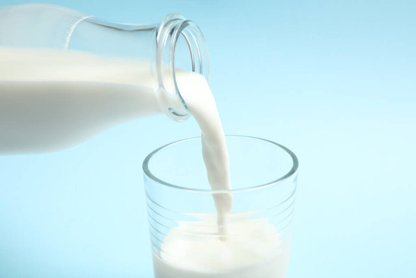 Pouring milk into glass on light blue background, closeup - Foto, afbeelding