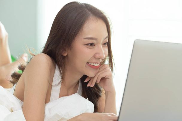 Asiatique femme travaillant sur un ordinateur portable assis sur le lit dans la maison. - Photo, image