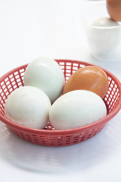 Gezouten ei en kippenei in plastic mandje op een witte ondergrond - Foto, afbeelding