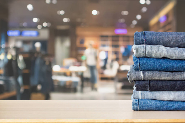 Blue denim jeans stack on wood table top with abstract blur clothing store in modern shopping mall defocused bokeh light background - Foto, Bild