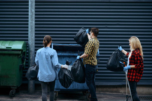 Εθελοντές βάζουν πλαστικές σακούλες σκουπιδιών στην ύπαιθρο, εθελοντικά. Οι άνθρωποι καθαρίζουν δρόμους της πόλης, οικολογική αποκατάσταση, συλλογή και ανακύκλωση απορριμμάτων, οικολογική φροντίδα, καθαρισμός περιβάλλοντος - Φωτογραφία, εικόνα