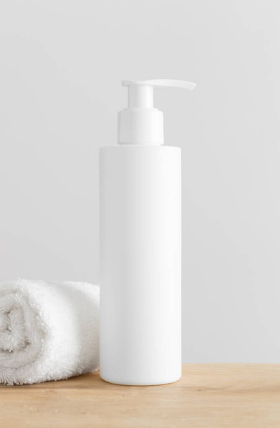 White cosmetic shampoo dispenser bottle mockup with a towel on a wooden table. - Φωτογραφία, εικόνα