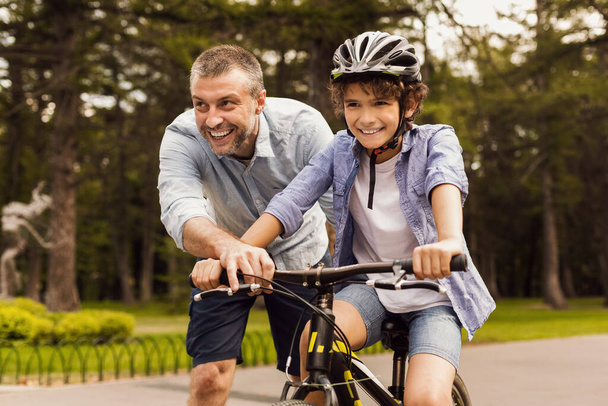 Αγόρι μαθαίνει ποδήλατο με τον ευτυχισμένο πατέρα του. - Φωτογραφία, εικόνα