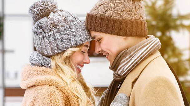 Ρομαντικό νεαρό ζευγάρι σε πλεκτά καπέλα αγγίζοντας τα μέτωπα κατά τη διάρκεια της χειμερινής ημερομηνίας σε εξωτερικούς χώρους - Φωτογραφία, εικόνα