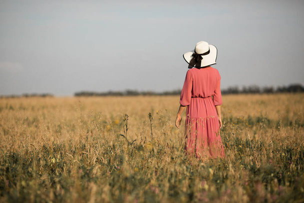 young woman in dress and hat in summer field - Foto, afbeelding