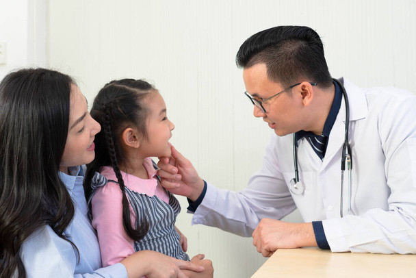 médico asiático mirando a la boca de chica joven que tiene dolor de garganta. pediatra y concepto de salud - Foto, imagen