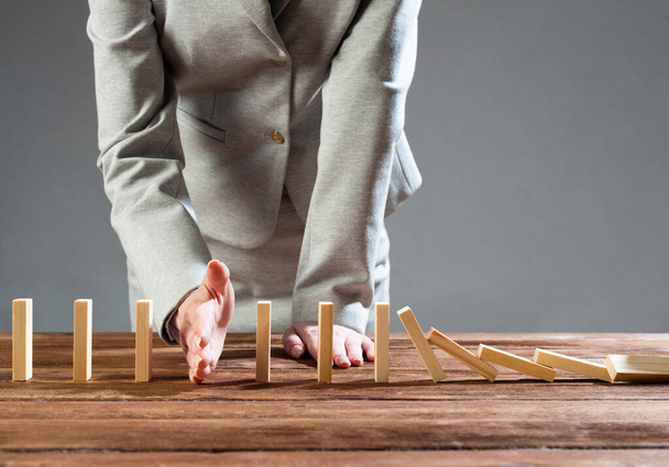 Businesswoman interrupting domino effect by stop falling wooden dominoes. Operative business solution, strategy and successful intervention. Business assistance, protection and prevention of crisis - Foto, imagen