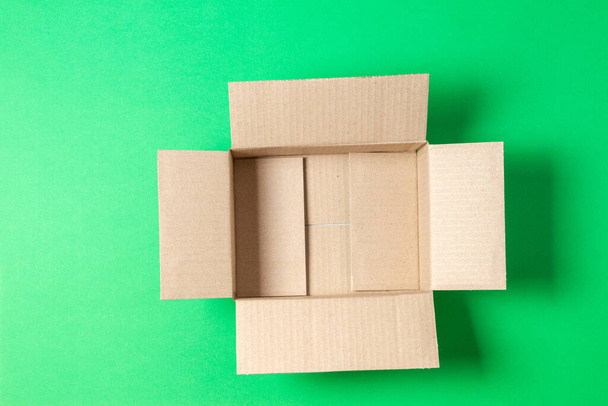 Одна пустая открытая коричневая картонная коробка на светло-зеленом фоне. Вид сверху - Фото, изображение