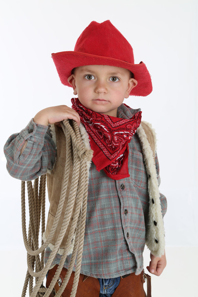 adorable young cowboy wearing a red hat and holding a rope - Фото, изображение