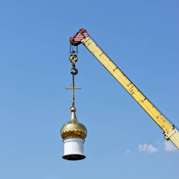 The dome of a Christian temple hangs on the hook of a crane. Building or dismantling a church against a blue sky. Symbolism - Photo, Image