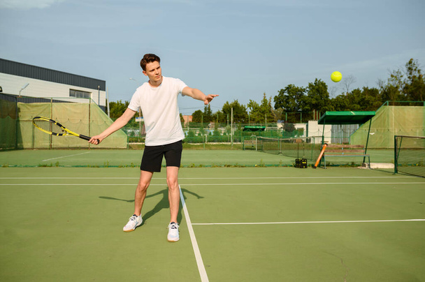 Male tennis player with racket hits the ball on outdoor court. Active healthy lifestyle, sport game competition, fitness training with racquet - Photo, Image