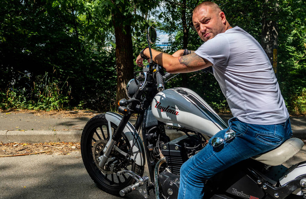 Junger gutaussehender Mann mit Tattoos und Bart und Armbändern auf dem Motorrad von Geon Daytona in Kiew - Foto, Bild