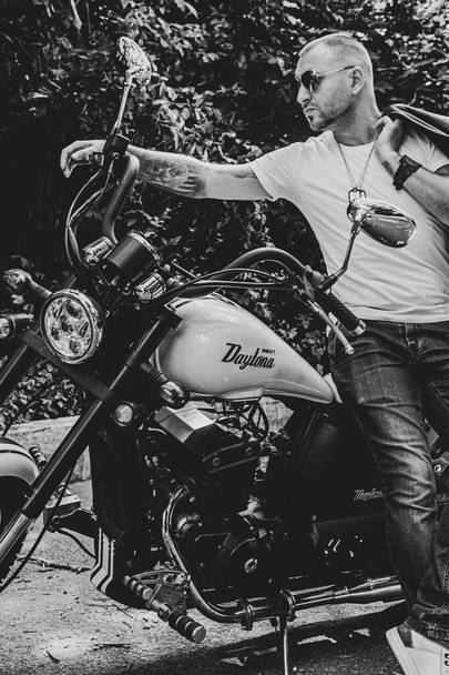 Jeune homme beau avec tatouages et barbe et bracelets sur la moto Geon Daytona à Kiev - Photo, image