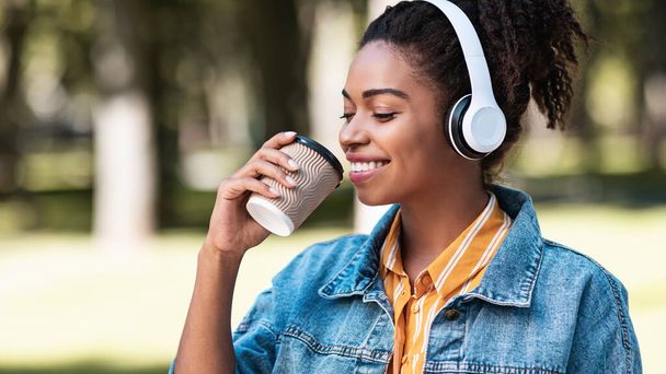 公園でコーヒーと音楽を楽しむ幸せな黒人女性 - 写真・画像