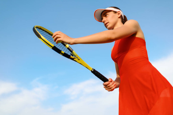 Теннисистка с ракеткой готовится ударить по мячу на открытой площадке. Активный здоровый образ жизни, спортивные соревнования, фитнес-тренировки с ракеткой - Фото, изображение