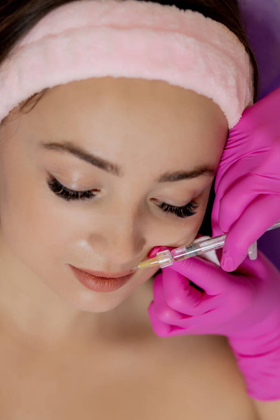 The doctor cosmetologist makes the Rejuvenating facial injections procedure for tightening and smoothing wrinkles on the face skin of a beautiful, young woman in a beauty salon - Photo, image