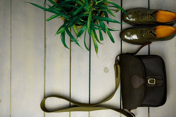 Groen gelakte oxford schoenen en crossbody tas op houten achtergrond in de buurt van bloempot. Bovenaanzicht. Sluit maar af. Kopieerruimte - Foto, afbeelding