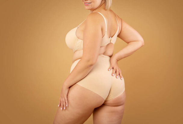 Giovane plus size donna in biancheria intima beige posa su sfondo studio marrone - Foto, immagini