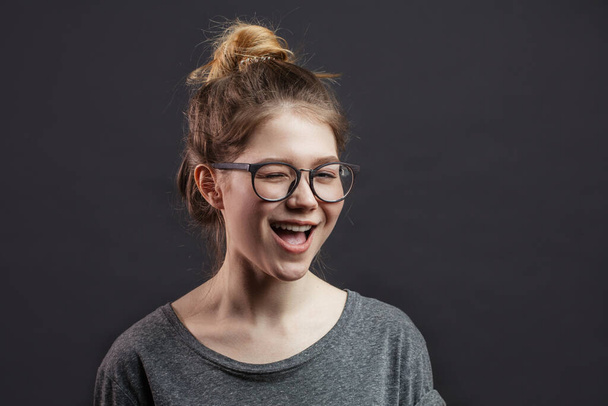Teenage gir beaming with happiness and screwing up her eyes against grey wall - 写真・画像