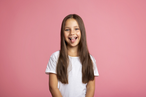 Ευτυχισμένο παιδί. Χαρούμενο μικρό παιδί που δείχνει γλώσσα, σε ροζ φόντο - Φωτογραφία, εικόνα