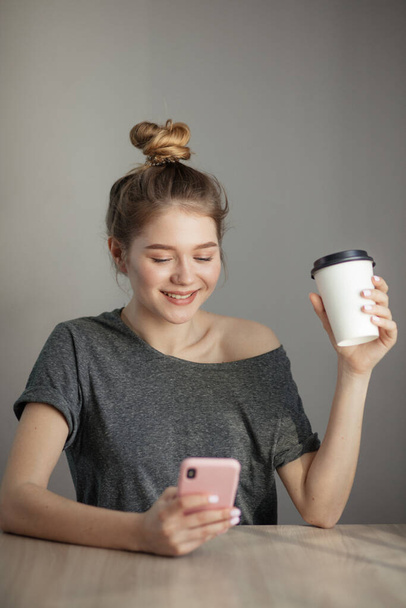 młoda kobieta siedząca przy stole z kawą przy użyciu telefonu komórkowego. - Zdjęcie, obraz