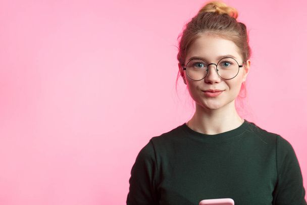 Portrait of a satisfied casual girl holding mobile phone isolated over pink background - Zdjęcie, obraz