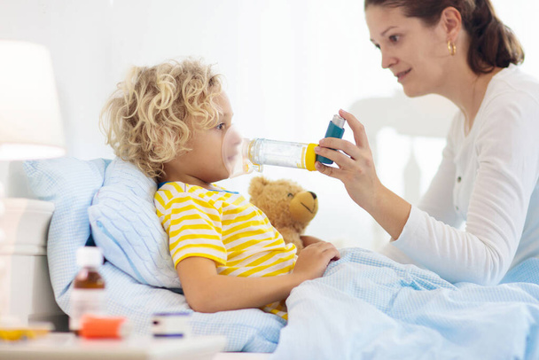 Sick little boy with asthma medicine. Mother with ill child lying in bed. Unwell kid with chamber inhaler for cough treatment. Flu season. Parent in bedroom or hospital room for young patient.  - Foto, immagini